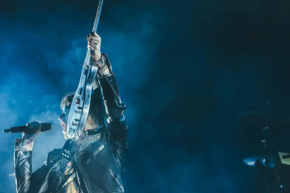 Musicien en blouson de cuir qui chante au micro en jouant de la guitare électrique sur une scène sombre