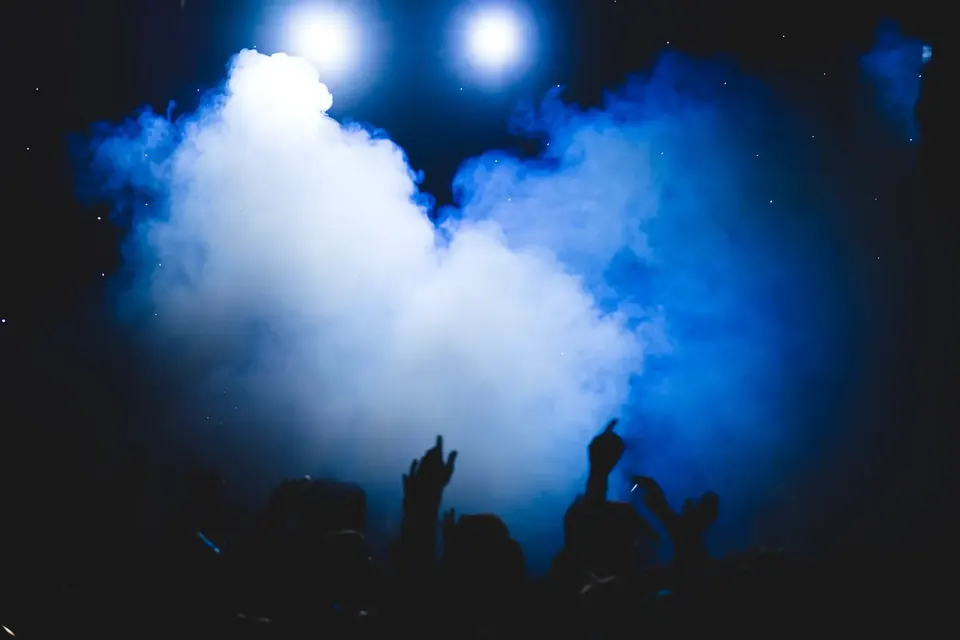 Scène de concert dans la fumée, éclairée de projecteurs colorés, silhouettes de musiciens