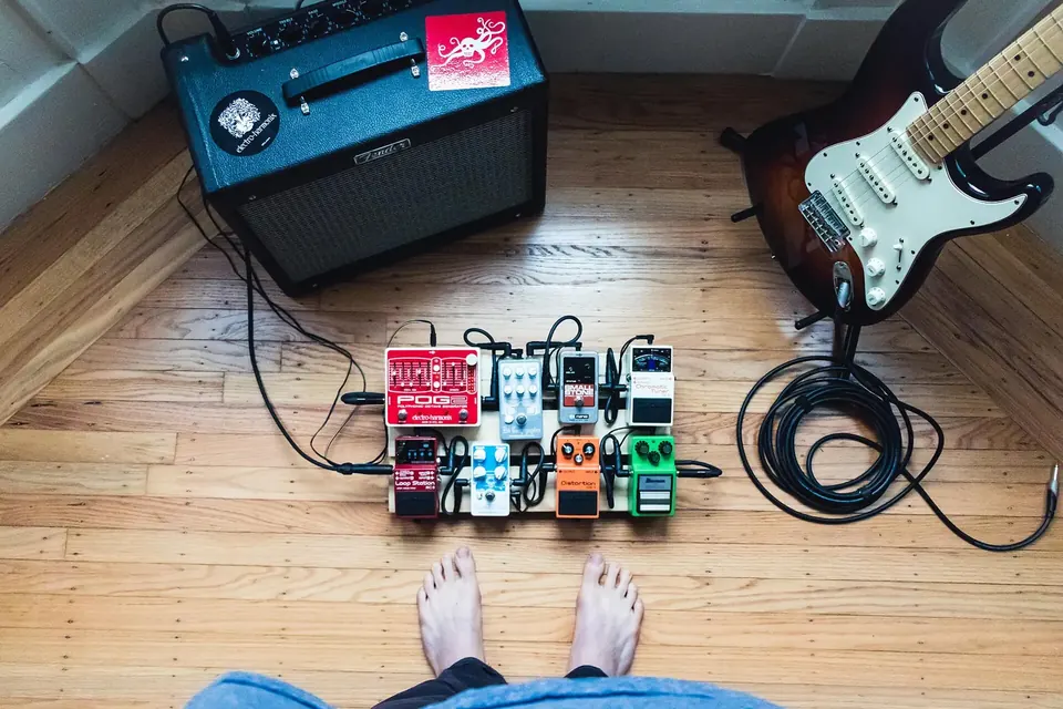Guitariste penché sur son matériel, pédales d'effets et câbles posés au sol